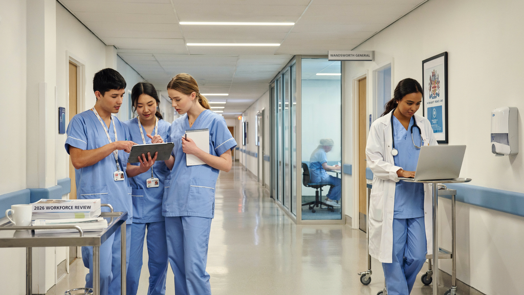 Three nurses on the left discussing their notes and a doctor on the right working on her laptop.